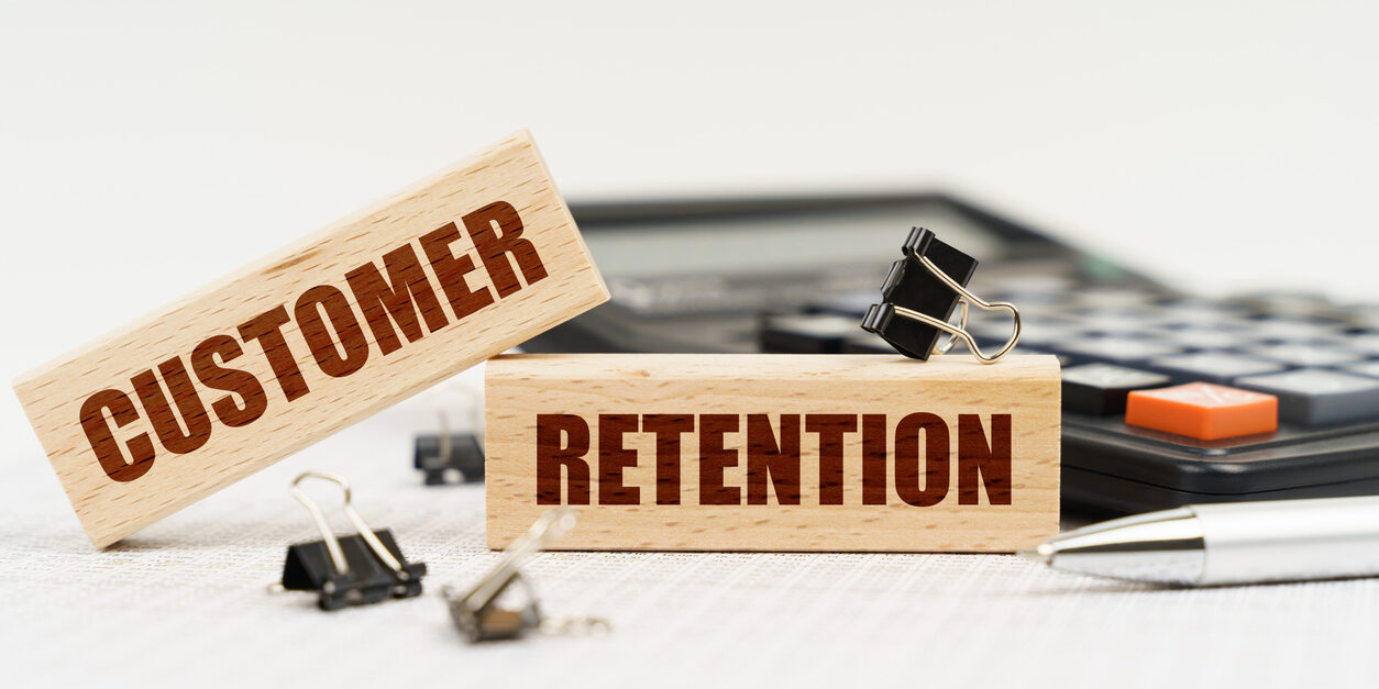 On a white background, a calculator, a pen, reports and wooden dies with the inscription – Customer Retention Business and finance concept. On a white background, a calculator, a pen, reports and wooden dies with the inscription - Customer Retention