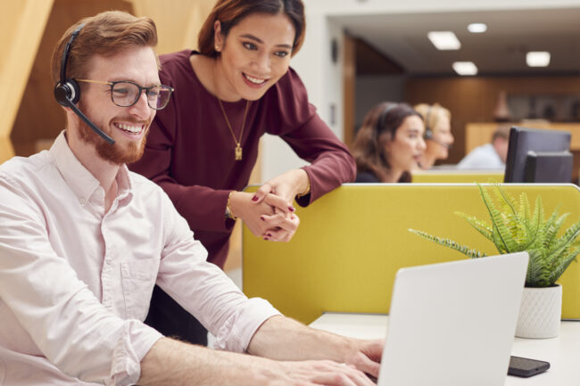 Businessman Wearing Headset Talking To Colleague In Busy Customer Services Center for customer experience management