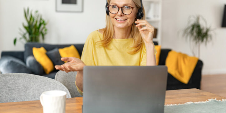 Smiling female call center employee using a headset and laptop for online communication with customers, a woman talking into microphone and gesturing