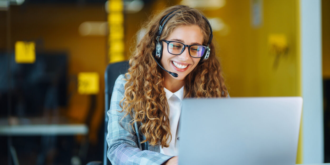 Call center agent with headset working on support hotline in modern office. Video conference.